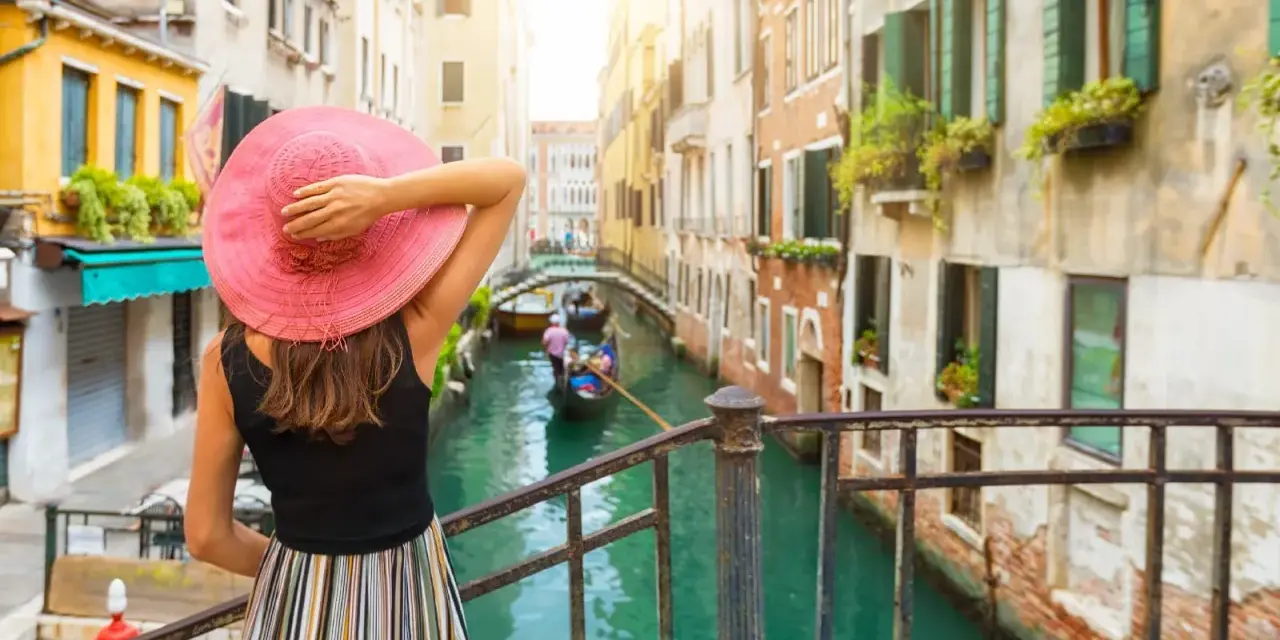 Una donna con cappello rosa ammira un canale a Venezia, un'esperienza indimenticabile di "Venezia in un giorno a piedi".