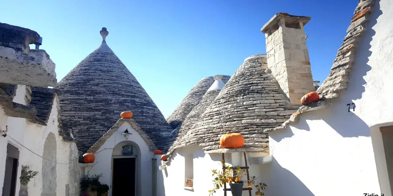 Trulli con zucche arancioni nel centro storico di Alberobello, sotto un cielo azzurro.