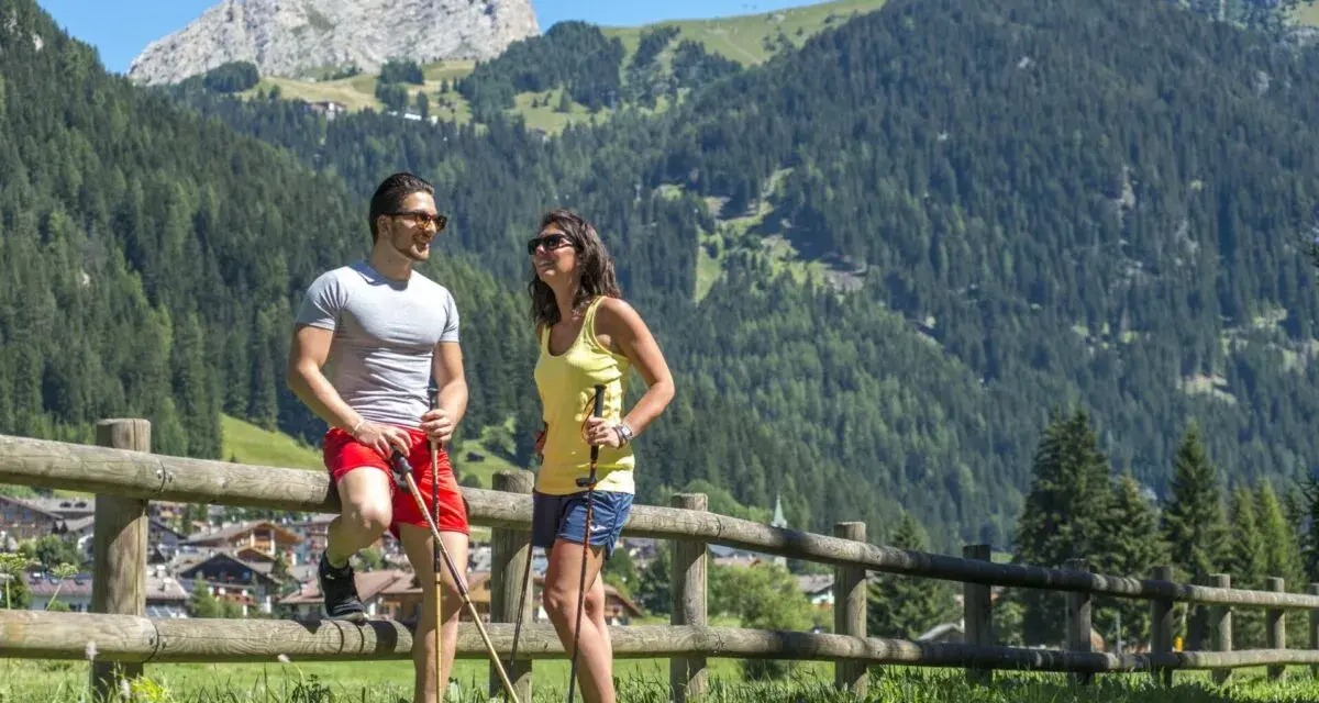 Coppia con bastoncini da trekking si gode il panorama montano, un'ottima idea per cosa fare a Canazei in estate.
