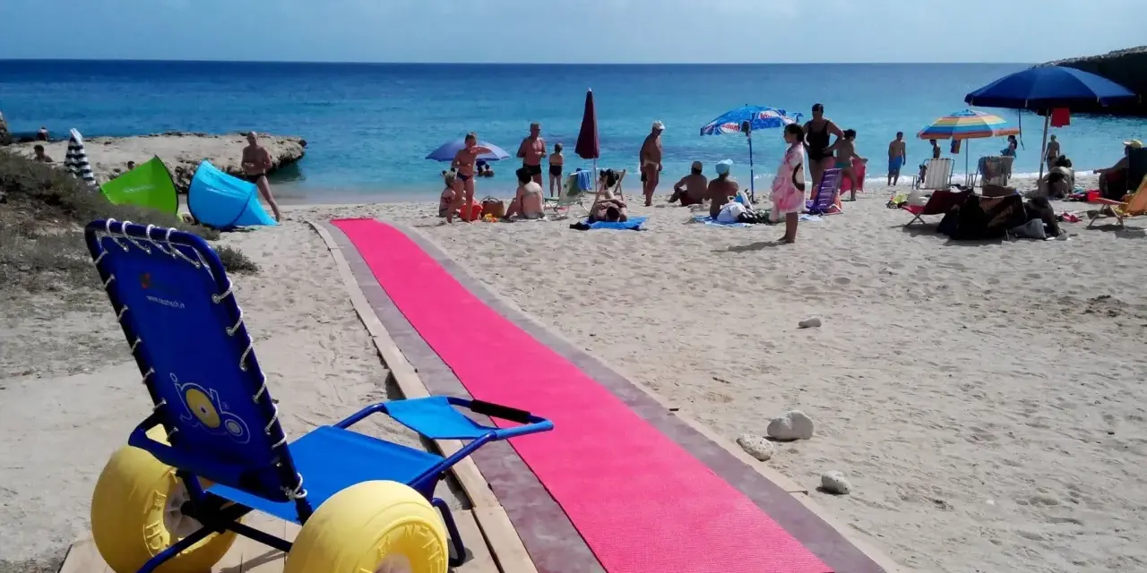 Una spiaggia attrezzata per gite per disabili, con una passerella rosa e una sedia a rotelle speciale per la sabbia.