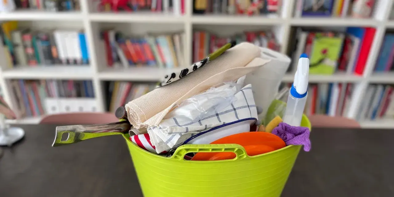 Secchio verde con accessori per la pulizia: rotolo di carta, panni, spruzzino, spugna. Ideale per sapere cosa portare in camper per un viaggio pulito.