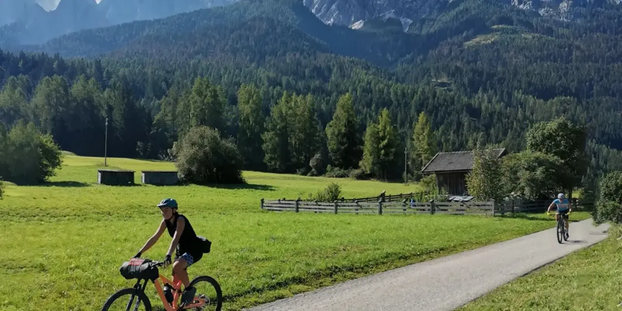Ciclisti lungo la ciclabile San Candido Lienz, tra prati verdi e montagne maestose. Un'avventura di chilometri immersi nella natura.