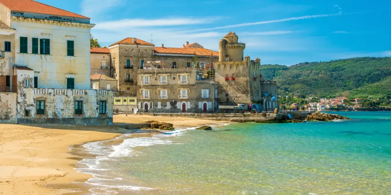 Spiaggia dorata e mare cristallino a Castellabate, con antichi palazzi e un castello che si affacciano sull'acqua. Un posto al mare da sogno.