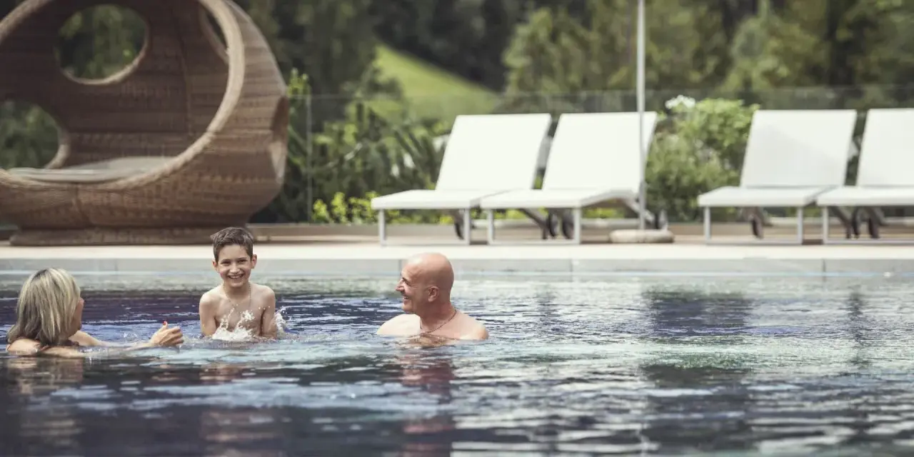 Famiglia felice si diverte in piscina al Cavallino Bianco Family Spa Grand Hotel. Relax e gioia per tutti.