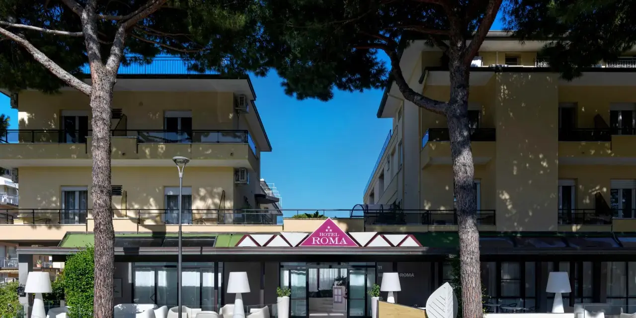 Hotel Roma Cesenatico, con pini marittimi e arredi esterni moderni, invita al relax.