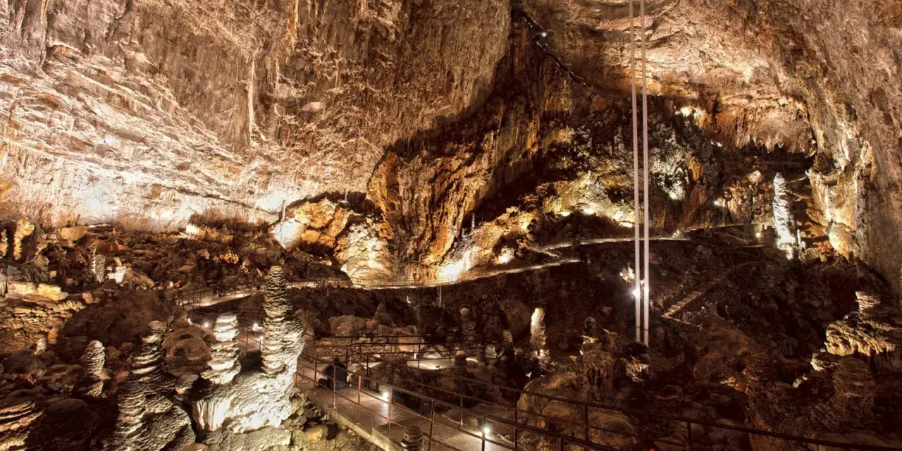 Sentiero illuminato tra stalattiti e stalagmiti in una delle magnifiche grotte in Italia. Un viaggio sotterraneo mozzafiato.