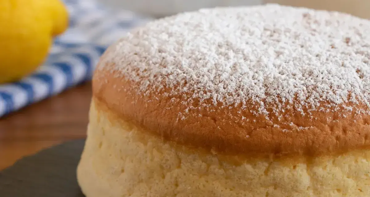Torta al vento mantovana soffice e leggera, cosparsa di zucchero a velo. Accanto, un limone e un tovagliolo a righe blu.