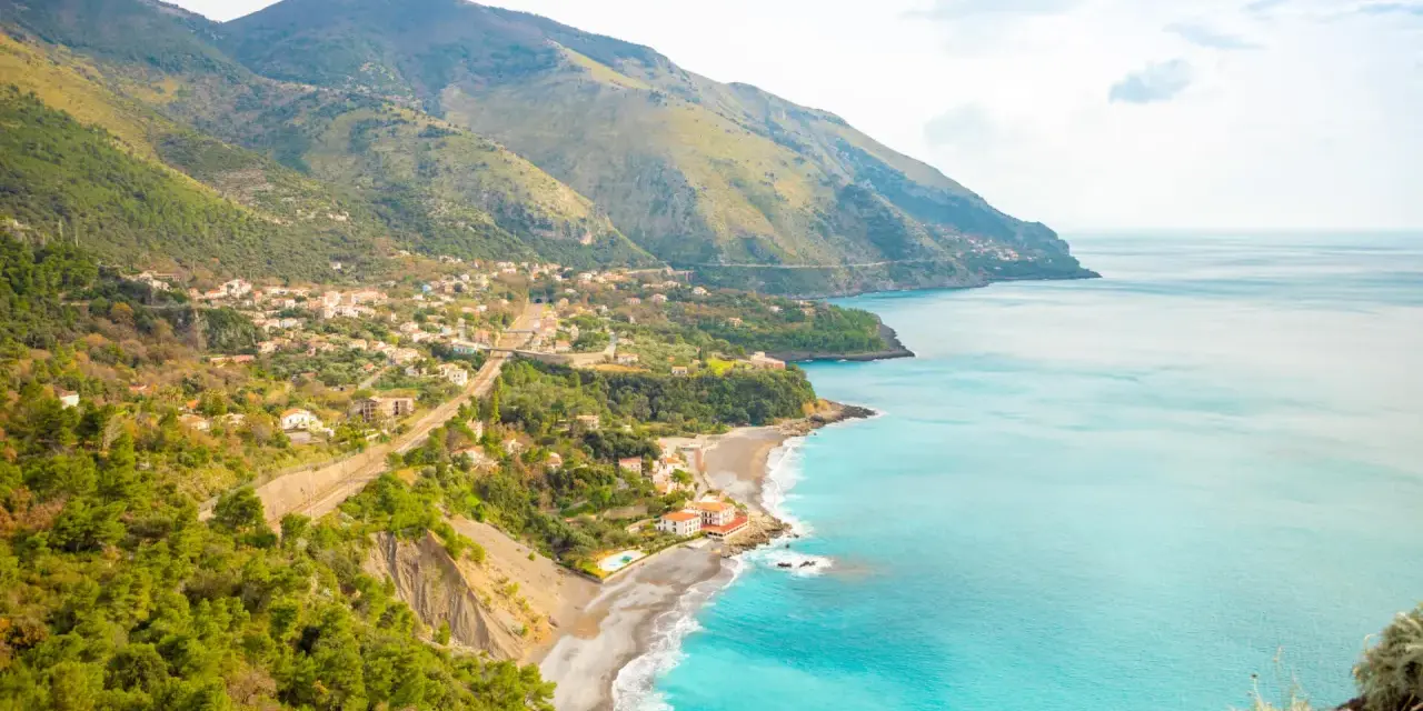 Panoramica di una costa montuosa con un villaggio affacciato sul mare turchese. Perfetto per itinerari Basilicata in macchina.