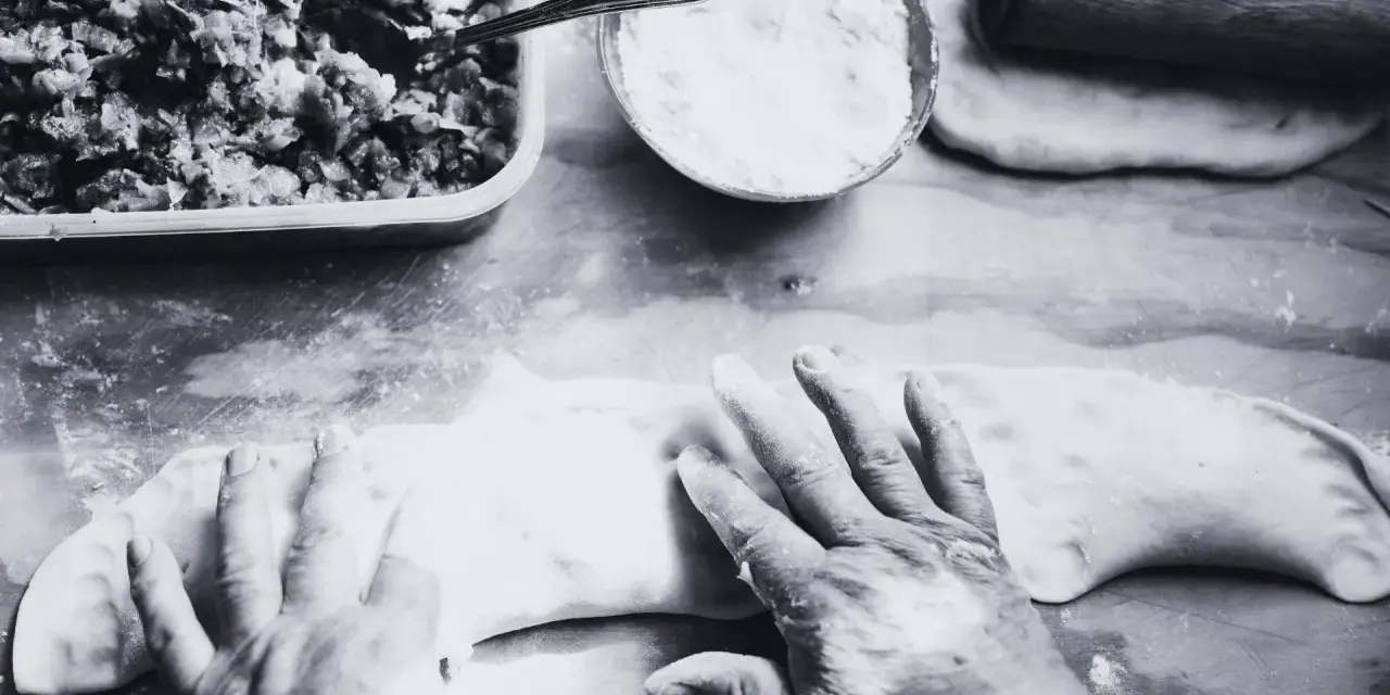 Mani esperte modellano la pasta per creare un'azdora romagnola, con ripieno e farina pronti.