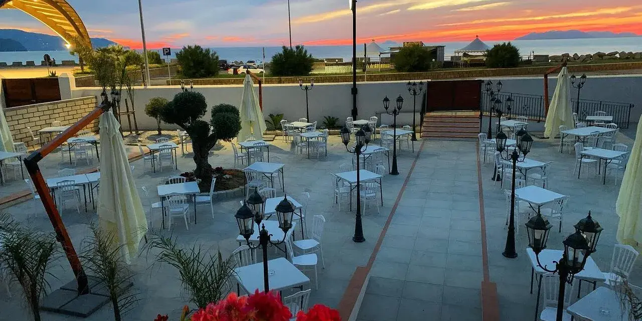 Terrazza di un ristorante al tramonto, con tavoli apparecchiati e fiori rossi. Un invito a scoprire il **vecchio palmento menu**.