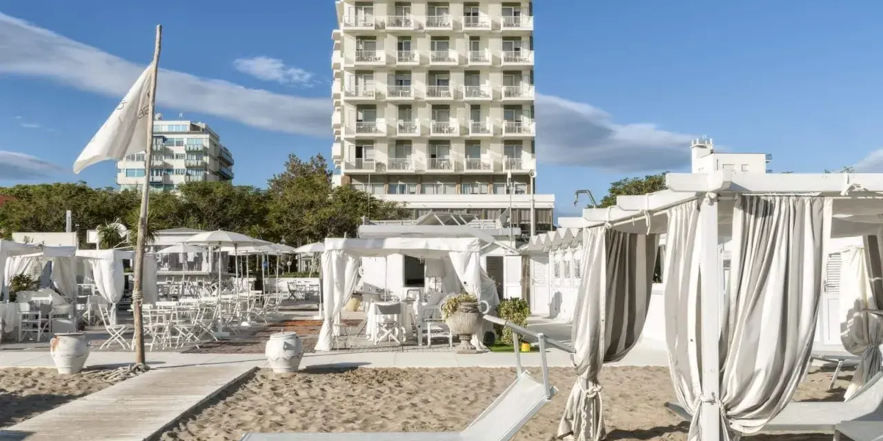 Spiaggia attrezzata con lettini e gazebo bianchi, sullo sfondo l'imponente hotel Abners.