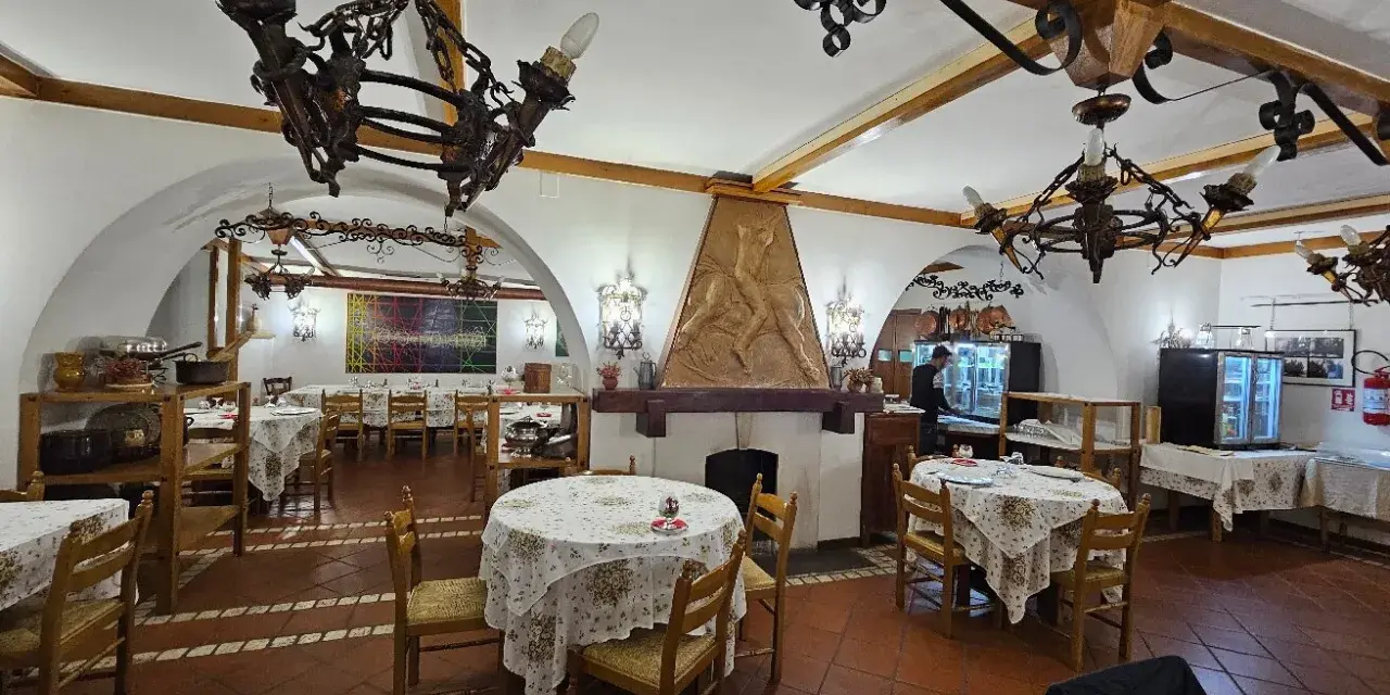 Interno di un ristorante con tavoli apparecchiati e un camino decorato. Un'ottima opzione per sapere dove mangiare a Potenza.