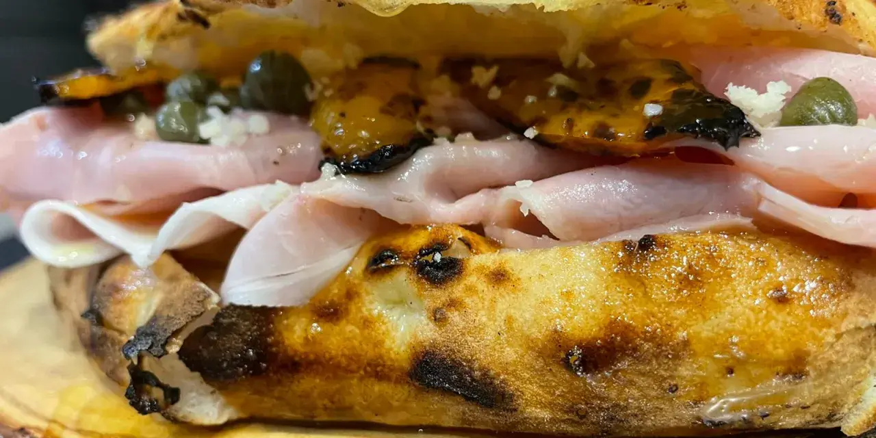 Un panino gourmet con mortadella, capperi e pomodori secchi, un vero re artù a Lecce, servito su un tagliere di legno.
