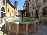 Fontana storica in pietra, un luogo incantevole tra le cose da vedere a Narni, con edifici antichi e un campanile sullo sfondo.