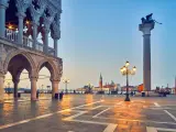 L'alba illumina il colonnato del Palazzo Ducale, proiettando lunghe ombre sulla piazza. In lontananza, il leone alato veglia su Piazza San Marco.