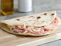 Piadina sfogliata romagnola ripiena di prosciutto cotto e formaggio, su tagliere di legno.
