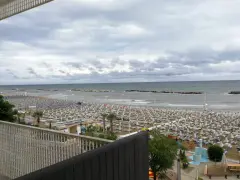 Spiaggia affollata di lettini e ombrelloni, con il mare calmo e il cielo nuvoloso. Vista dal piccadilly hotel bellaria.