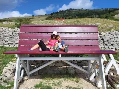 Gita domenicale con bambini nel Lazio: mamma e figlio si godono il panorama su una panchina gigante, con montagne e cielo azzurro sullo sfondo.