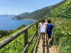 Bambini esplorano i sentieri panoramici delle Cinque Terre, con il mare blu e la vegetazione rigogliosa.