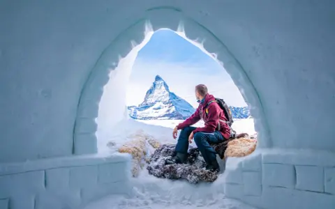 Un uomo ammira il maestoso Cervino dall'interno di un igloo, un'esperienza unica di dormire in un igloo in Italia.