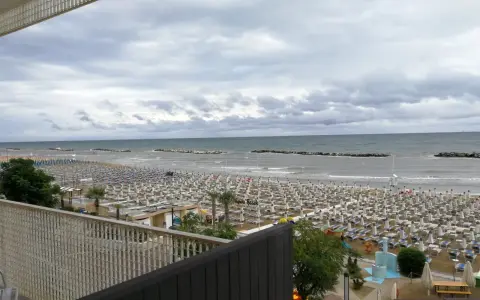 Spiaggia affollata di lettini e ombrelloni, con il mare calmo e il cielo nuvoloso. Vista dal piccadilly hotel bellaria.