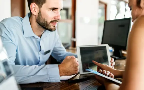 Receptionist con tablet mostra a cliente che non ci sono più camere, un caso di overbooking hotel.