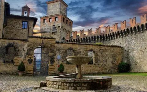 Cortile di uno dei castelli vicino Parma, con fontana in pietra e mura merlate sotto un cielo drammatico.
