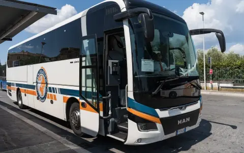 Autobus FlixBus pronto a partire da Agropoli per Roma. Il mezzo bianco con strisce arancioni e blu attende i passeggeri sotto un cielo azzurro.