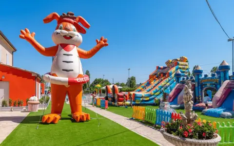 Gigante coniglio gonfiabile "Ciccio" accoglie i bambini in un parco giochi con scivoli e castelli gonfiabili, un'oasi di divertimento per gli ospiti dell'hotel Ciccio.
