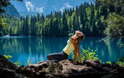Donna in posa yoga su rocce, con lago turchese e montagne sullo sfondo. Un'immagine di serenità nella friuli montagna estate.