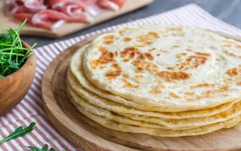 Pila di piadine marchigiane, pronte per essere farcite con rucola e salumi.