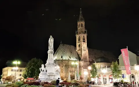 Piazza Walther di Bolzano di notte: la cattedrale, il monumento e la bandiera rossa. Un'idea di cosa vedere a Bolzano in un giorno.