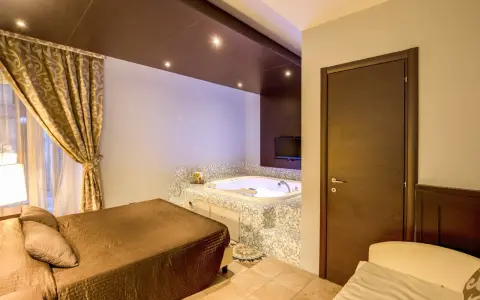 Camera con vasca idromassaggio e letto matrimoniale al **hotel The Strand**. Tende dorate e TV a parete.