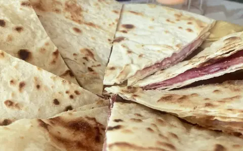 Piadina sfogliata ricetta originale, con strati sottili e ripieno di salumi, pronta per essere gustata.