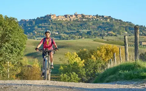 Ciclista su strada sterrata con borgo medievale sullo sfondo, un'incantevole ciclabile toscana.