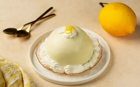 Dolce al limone, perfetto per scoprire cosa mangiare a Salerno. Servito con panna e scorzetta, pronto per essere gustato con cucchiaini dorati.