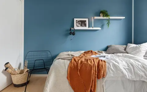 Camera da letto moderna con letto, coperta arancione, cestino e sedia in metallo. Utile per la classificazione camere hotel.