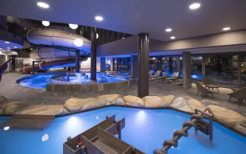 Piscina interna con scivoli acquatici e giochi d'acqua al Quellenhof Merano, un'oasi di divertimento e relax.
