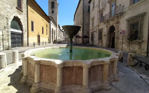Fontana storica in pietra, un luogo incantevole tra le cose da vedere a Narni, con edifici antichi e un campanile sullo sfondo.