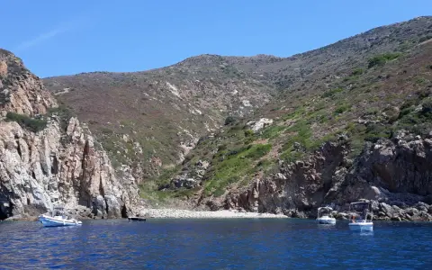 Barche a vela nella cala del corvo, con scogliere rocciose e vegetazione mediterranea.
