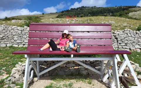 Gita domenicale con bambini nel Lazio: mamma e figlio si godono il panorama su una panchina gigante, con montagne e cielo azzurro sullo sfondo.