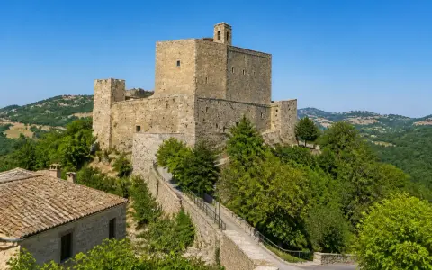 Rocche imponenti e case in pietra a Montefiore Conca, circondate da verdi colline sotto un cielo azzurro.
