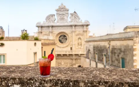 Cocktail rosso con fragola e menta, sullo sfondo la Basilica di Santa Croce. Il miglior aperitivo a Lecce.