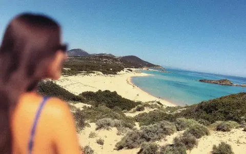 Vista mozzafiato di una spiaggia sarda, con dune sabbiose e macchia mediterranea. Perfetta per le gite in Sardegna.