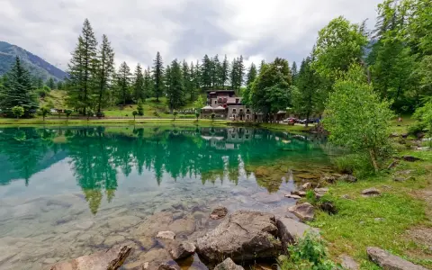 Lago alpino con riflessi verdi, perfetto per le gite in Piemonte. Case e alberi incorniciano la riva.