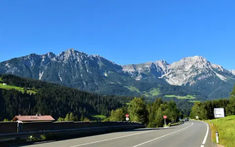 Strada panoramica per viaggi in auto in Europa dall'Italia, con montagne imponenti e boschi verdi.