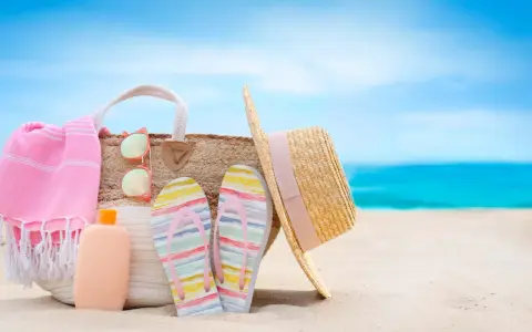 Borsa da spiaggia con asciugamano rosa, infradito colorate, occhiali da sole e cappello di paglia. Ecco cosa portare al mare per una giornata perfetta!