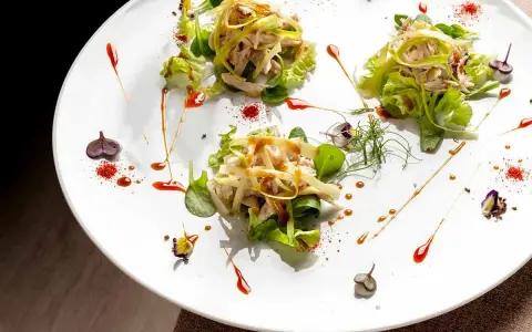 Tre porzioni di insalata di pollo e verdure su un piatto bianco, un'ottima opzione per trattorie economiche a Bra.