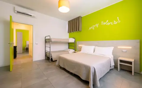 Camera luminosa con letto matrimoniale, letto a castello e parete verde brillante. Un invito a godersi i colori del green village Cesenatico.