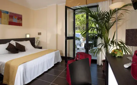 Camera accogliente al Park Hotel Kursaal Misano, con letto comodo, piante verdi e valigie rosse pronte per la partenza.